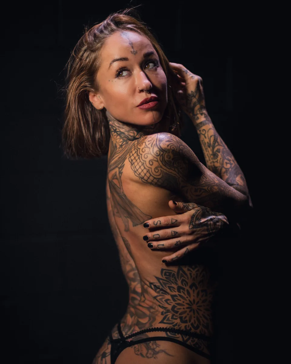 Low-key studio portrait of a tattooed model turning over one shoulder against a black background