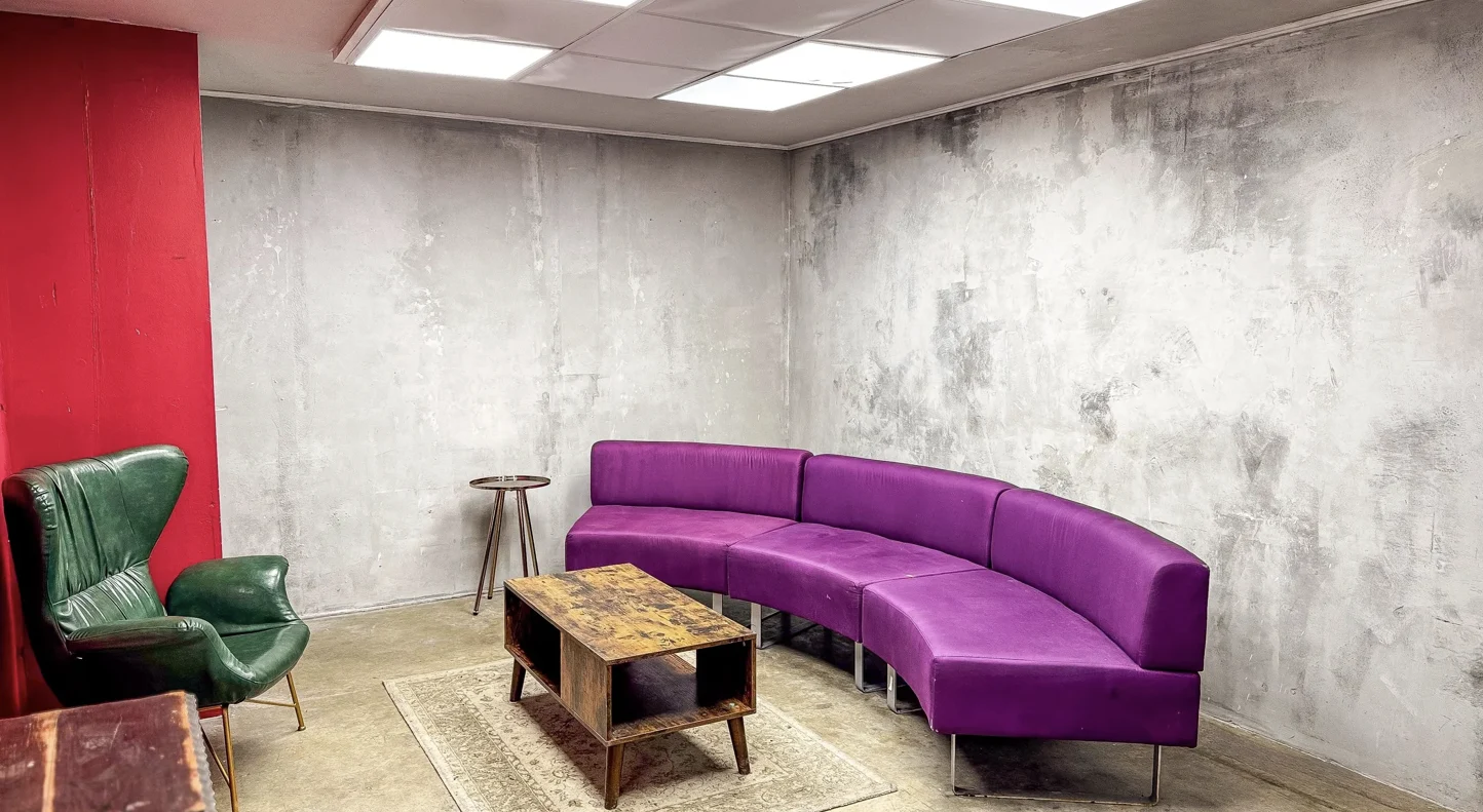 Studio lounge with a curved purple sofa, green chair and textured walls